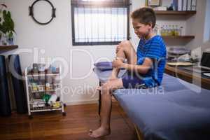 Boy frowning with knee pain while sitting on bed