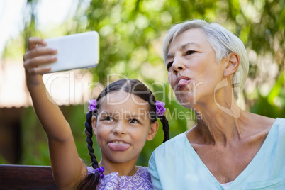 Girl and grandmother sticking out tongue while taking selfie