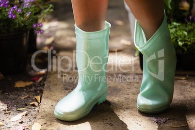 Low section of girl wearing green rubber boot standing on footpath