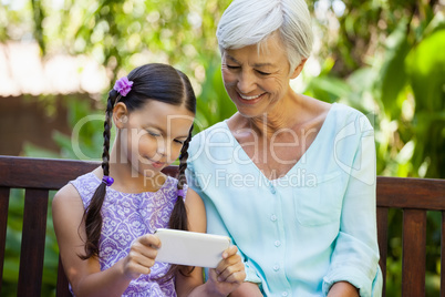 Smiling senior woman looking at girl using mobile phone
