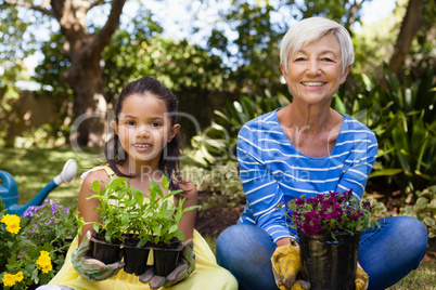 Portrait of smiling girl and granddaughter sitting while holding plants