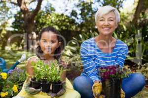 Portrait of smiling girl and granddaughter sitting while holding plants
