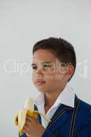 Schoolboy eating banana against white background