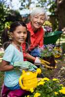 Portrait of smiling senior woman and girl watering flowers
