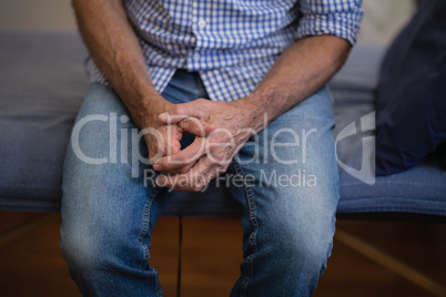 Midsection of senior male patient sitting with hands clasped on bed