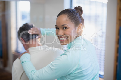 Rear view of portrait of smiling female therapist giving neck massaging to senior male patient