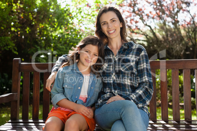 Portrait of smiling beautiful woman and daughter sitting on wooden bench