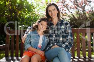 Portrait of smiling beautiful woman and daughter sitting on wooden bench