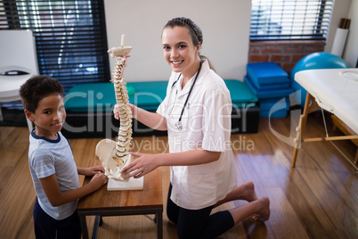 Side view portrait of smiling female therapist and boy kneeling with artificial spine