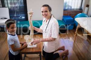 Side view portrait of smiling female therapist and boy kneeling with artificial spine