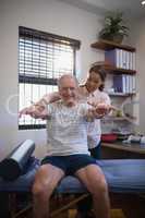 Female doctor looking at smiling senior male patient with arms raised