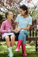 Smiling mother and daughter reading novel while sitting on bench