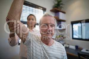 Senior man looking away while female doctor examining elbow