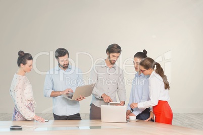Business people at a desk looking at computers and tablets against white wall