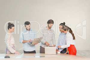 Business people at a desk looking at computers and tablets against white wall