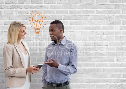 Happy business people talking against white wall with bulb graphic