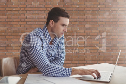Business man at a desk using a computer against brick wall