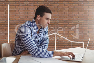 Business man at a desk using a computer against brick wall with graphics