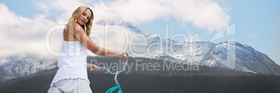 Woman looking over shoulder on bicycle against snowy mountain with trees