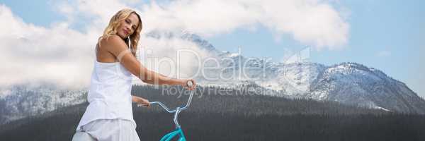 Woman looking over shoulder on bicycle against snowy mountain with trees