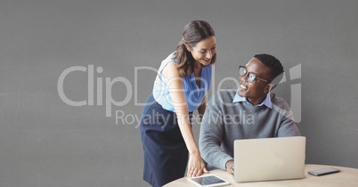 Happy business people at a desk using a computer against grey background