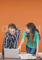 Business people at a desk pointing at a computer against orange background