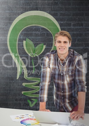 Happy business man at a desk standing against black wall with green bulb graphic