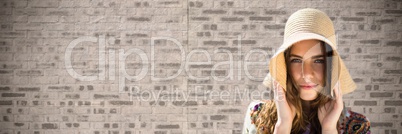 Portraiture of woman holding sun hat against brown brick wall