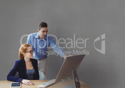 Business people at a desk looking at a computer against grey background