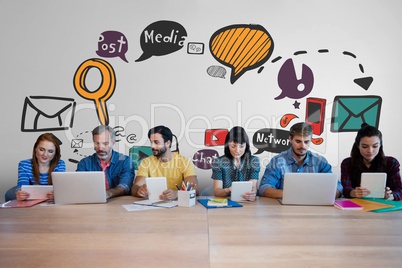 Business people at a desk looking at computers and tablets against white wall with graphics