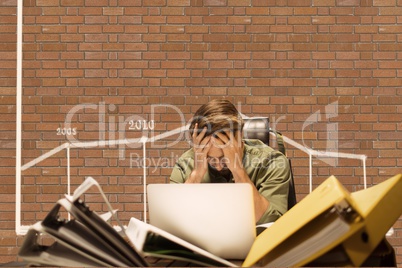 Frustrated business man at a desk sitting against brick wall with graphics