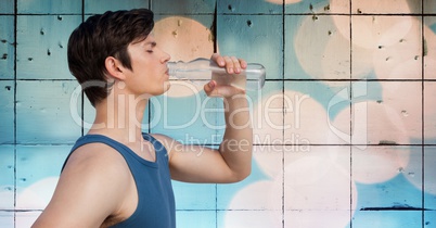Man in training gear drinking water against tiles and bokeh