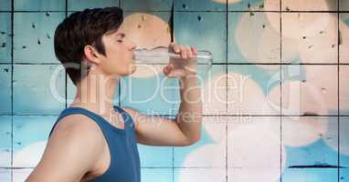 Man in training gear drinking water against tiles and bokeh