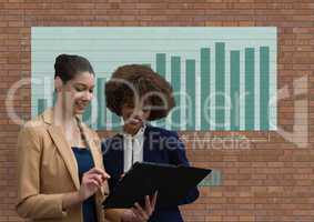 Happy business women using a tablet against brick wall with graphics