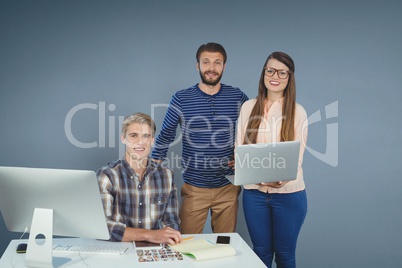 Happy business people at a desk standing with a tablet and a computer against blue background