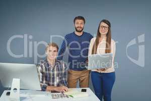 Happy business people at a desk standing with a tablet and a computer against blue background