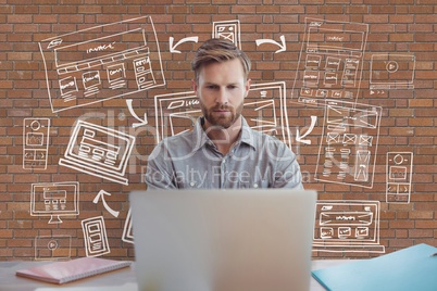 Business man at a desk using a computer against brick wall with graphics