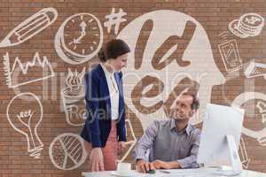 Happy business people at a desk using a computer against brick wall with graphics