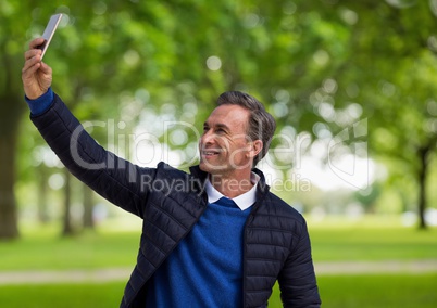 Middle aged man taking selfie against blurry trees