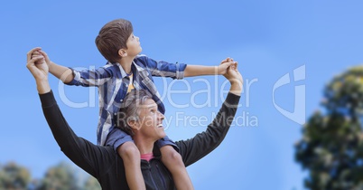 Father with son on shoulders against sky and blurry trees