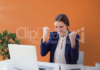 Excited business woman at a desk looking at a computer against orange background