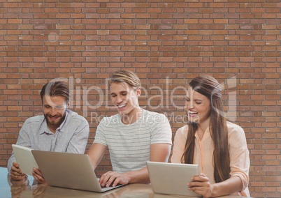 Happy business people at a desk looking at a computer and a tablet against brick wall
