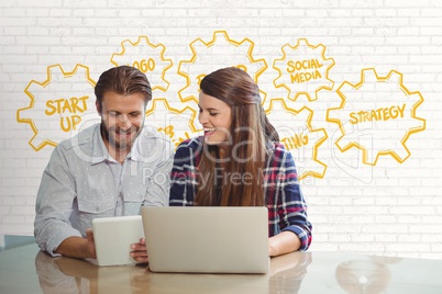 Happy business people at a desk looking at a tablet and a computer against white wall with yellow gr