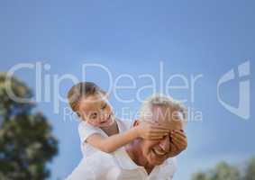 Girl and grandfather piggyback against sky and blurry trees