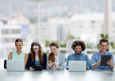 Happy business people at a desk looking at phones, computers and tablets