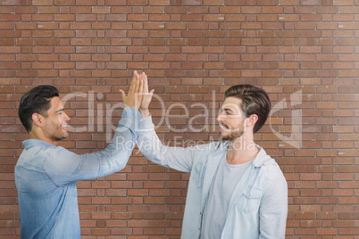 Happy business men doing a high five against brick wall