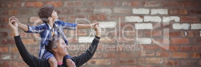 Father with son on shoulders against blurry red brick wall