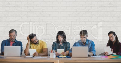Business people at a desk looking at computers and tablets against white wall