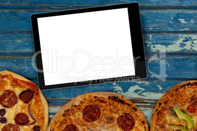 Blank tablet device on table above three pizzas