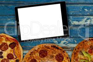Blank tablet device on table above three pizzas